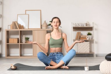 Güzel genç bir kadın evde meditasyon yapıyor.