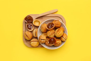 Kase ve ahşap tahta tahta ceviz şekilli kurabiyeler ve sarı arka planda kaynamış konsantre süt.