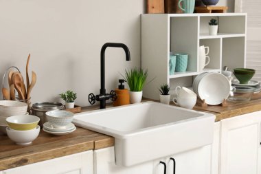 Şık seramik lavabo, temiz bulaşıklar ve ahşap mutfak tezgahındaki raf ünitesi.