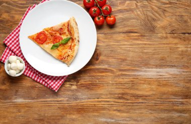 Lezzetli bir dilim pizza, Margarita ve ahşap arka planda malzemeler.