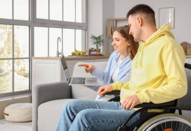 Tekerlekli sandalyedeki genç adam ve evinde dizüstü bilgisayarı olan kız arkadaşı.