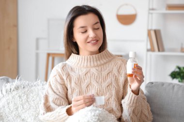 Evdeki kanepede öksürük şurubuyla oturan hasta genç kadın.