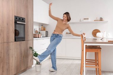 Genç kadın mutfakta dans ediyor.
