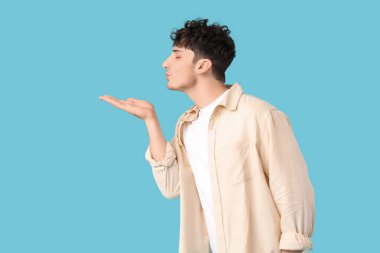 Yakışıklı genç adam mavi arka planda öpüşüyor.