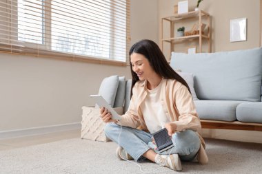Evde tablet bilgisayar kullanan, modern güç bankası olan güzel genç bir kadın.
