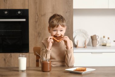 Yüzünde çikolata ezmesi olan tatlı bir çocuk mutfakta tatlı tost yiyor.