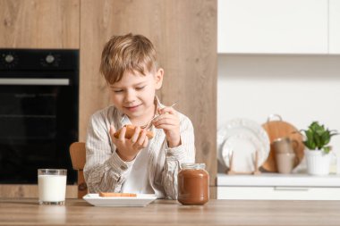 Mutfakta tatlı çikolata ezmesi dolu bir kavanozla tost yapan sevimli küçük çocuk.