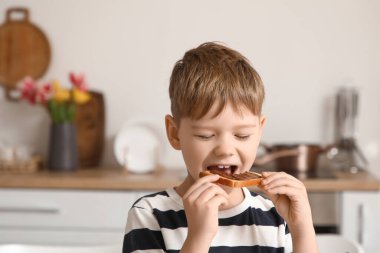 Mutfakta çikolata ezmeli tost yiyen tatlı küçük çocuk.