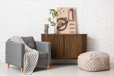 Bambu saplı vazo, şık koltuk ve hafif tuğla duvarın yanında puf.