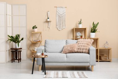 Oturma odasının içinde kanepe, raf ve yeşil bitkiler var.