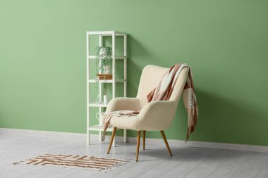 Yumuşak ekoseli şık beyaz koltuk ve yeşil duvarın yanındaki raf.