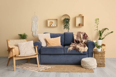 Oturma odasının iç tarafındaki bej duvarın yanında mavi kanepe, puf ve koltuk.