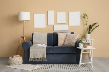 Mavi kanepe, yer lambası ve oturma odasının iç tarafındaki bej duvarın yanındaki bitkiler.