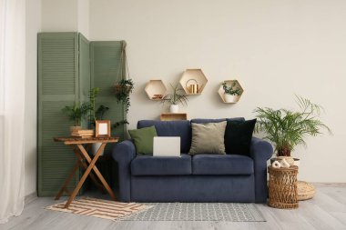 Mavi kanepe, katlanır ekran ve oturma odasının içindeki beyaz duvarın yanındaki masa.