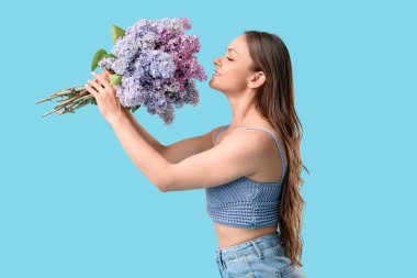 Beautiful young woman with bouquet of blooming lilac flowers on blue background