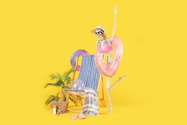 Kumsal aksesuarları ve sarı arka planda iskele koltuğu olan insan iskeleti.