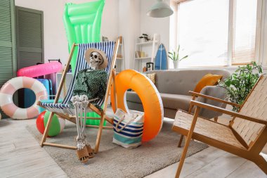 Güverte sandalyesinde insan iskeleti ve oturma odasında plaj aksesuarları.