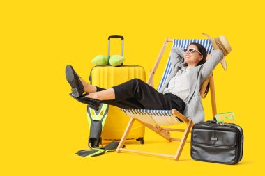 Güverte koltuğunda genç bir iş kadını ve sarı arka planda plaj aksesuarları. Yaz tatili kavramı