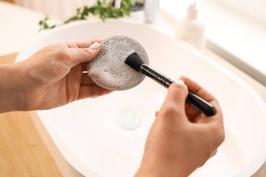 Kadın elleri makyaj fırçasını lavabonun üstünde aletle yıkıyor.