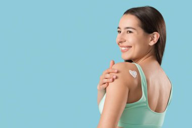 Mavi arka planda güneş kreminden yapılmış kalbi olan genç bir kadın.