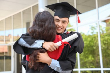 Mezuniyet gününde kucaklaşan diplomalı iki öğrenci.