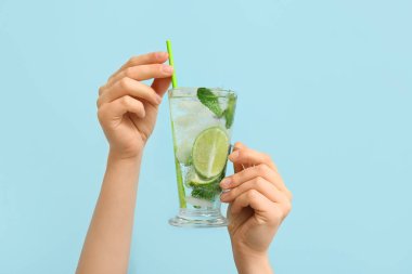Mavi arka planda cam bardak taze Mojito kokteyli olan kadın elleri.
