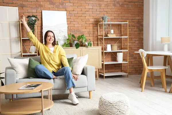 Evdeki gri kanepede oturan mutlu genç kadın.