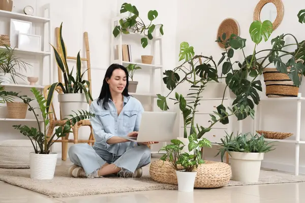 Evde dizüstü bilgisayarı ve çiçekleri olan güzel bir kadın.