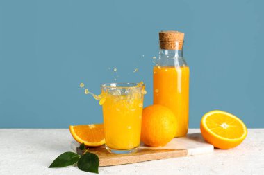 Şişe ve bir bardak taze portakal suyu. Masada mavi arka planda su sıçraması var.