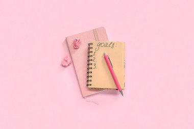 Liste yapmak için boş defterler ve pembe arka planda kalem. Yeni yıl hedefleri