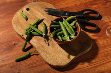 Yeni kesme tahtası, makas ve ahşap zemin üzerinde yeşil bezelye kabı