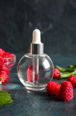 Arka planda bir şişe kozmetik ahududu yağı.