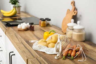 Mutfaktaki tezgahta farklı taze sebzelerle örgü torbaları var.