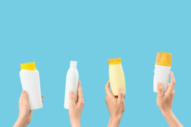 Mavi arka planda güneş kremi şişeleri olan kadın elleri