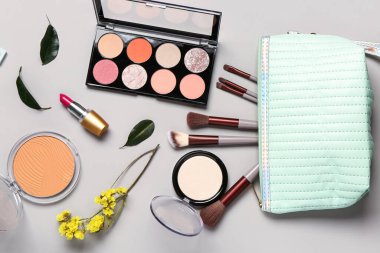 Makyaj ürünleri ve gri arka planda güzel çiçeklerle süslü bir makyaj çantası.