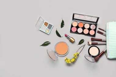 Makyaj ürünleri ve gri arka planda güzel çiçeklerle süslü bir makyaj çantası.