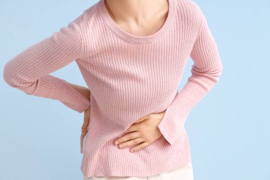 Mavi arka planda karın ağrısı çeken genç bir kadın, yakın plan.