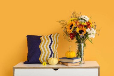 Sonbahar çiçekleri ve turuncu duvarın yanında balkabakları olan çekmeceler.