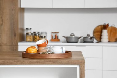 Modern mutfaktaki ahşap tepside çay seti ve tarçın rulosu, yakın plan.