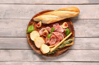 Lezzetli jambon, fesleğen, ekmek, İtalyan Grissini ve gri ahşap arkaplanda incir dilimleri.