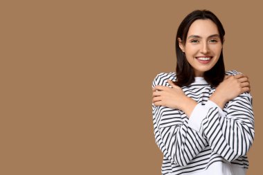 Kahverengi arka planda kendine sarılan genç bir kadın.