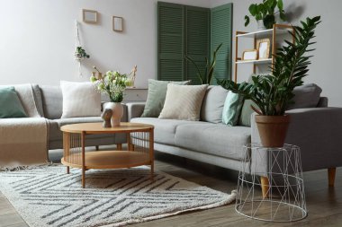 Gri kanepeleri, kahve masasında vazosu ve çiçekleri olan modern oturma odasının içinde.