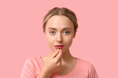 Genç bir kadın pembe arka planda A vitamini hapı alıyor, yakın plan.