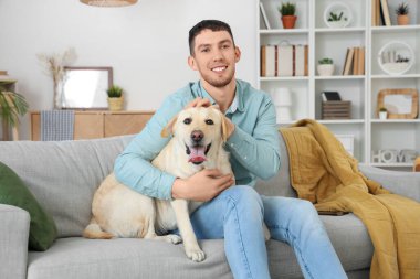 Labrador köpeği olan genç adam evdeki kanepede oturuyor.