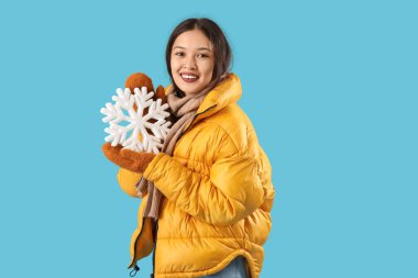 Mavi arka planda kar taneleri olan sıcak eşarplı güzel Asyalı bir kadın.