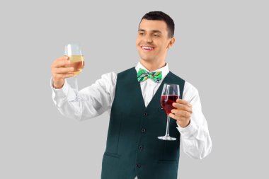 Gri arka planda şarap kadehleri olan genç barmen.