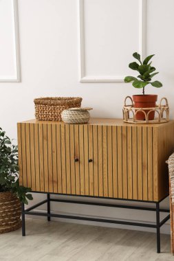 Beyaz duvarın yanında saksı ve hasır sepetli ahşap dolap.