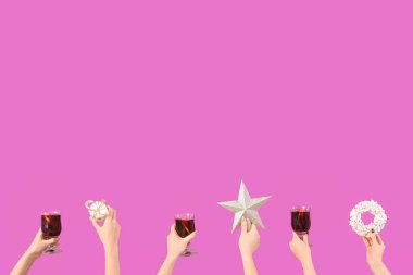 Sıcak şarap kadehleriyle kadın elleri ve pembe arka planda Noel dekoru.