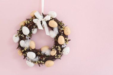 Güzel Paskalya çelengi pembe duvarda yumurta ve tüyle süslenmiş.