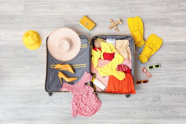 İçinde kadın kıyafetleri, güneş kremi ve yüzgeçler olan açık bir bavul. Seyahat kavramı